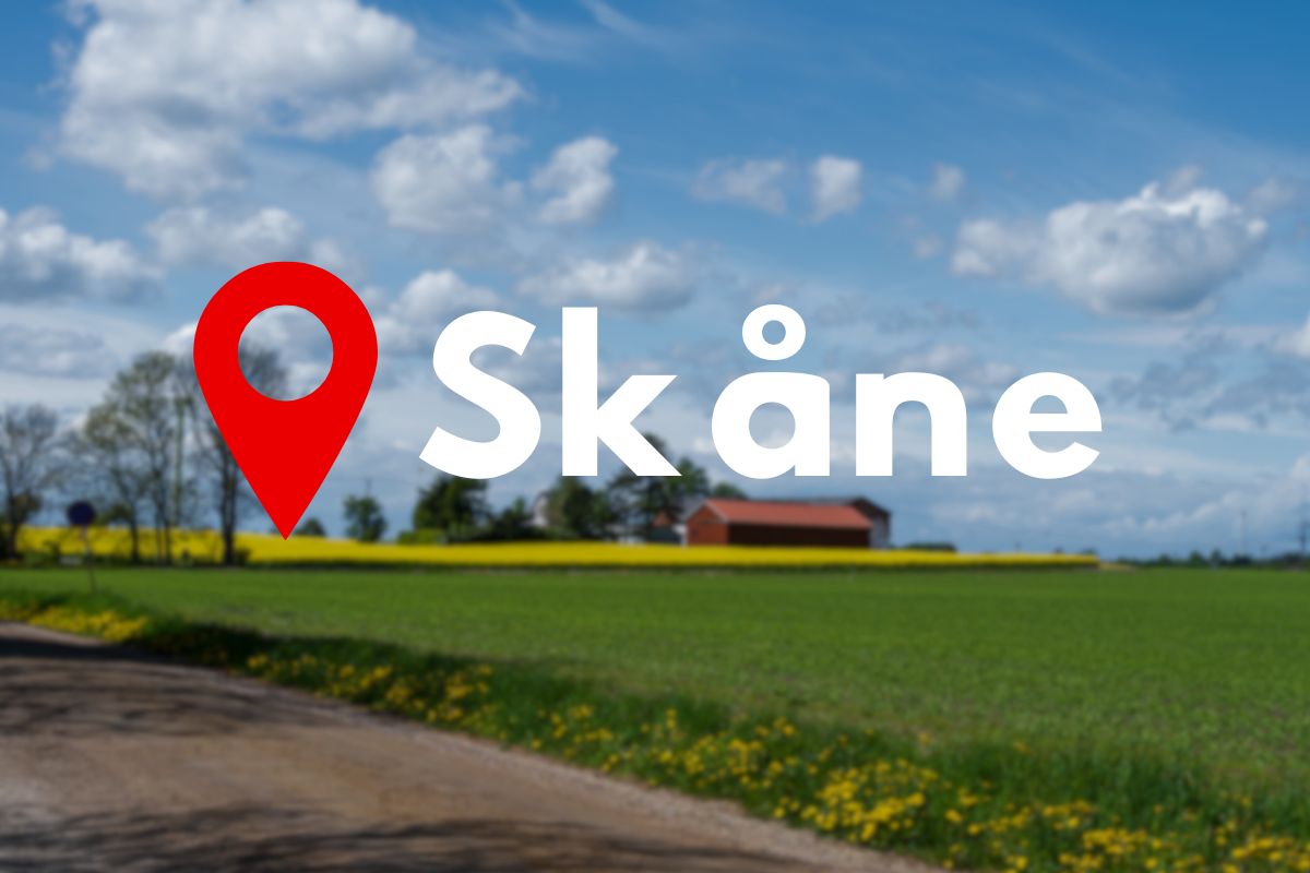 Skånskt landskap med rapsfält och en stor röd platsmarkör med texten "Skåne"