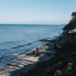Två personer som går på strand intill berg som reser sig