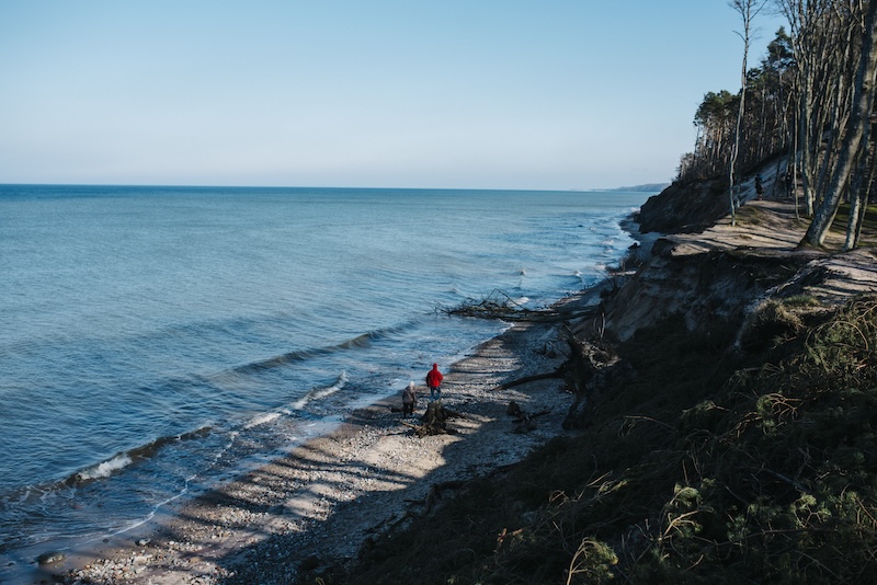 Två personer som går på strand intill berg som reser sig
